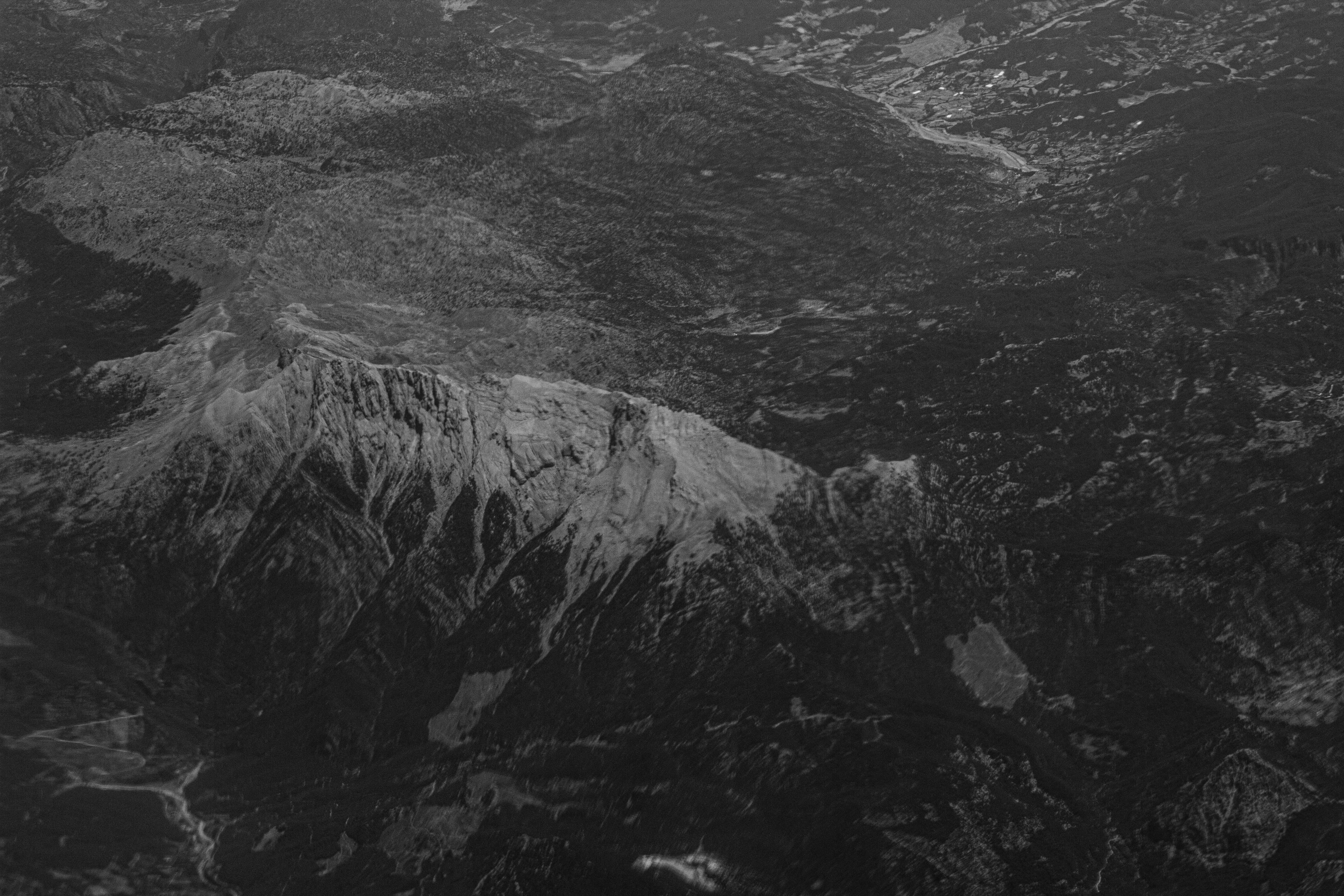 Mountain terrain from aerial view, rugged rocky landscape with dark shadows and atmospheric depth, dim natural lighting