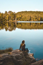 a person sitting on a rock near a lake