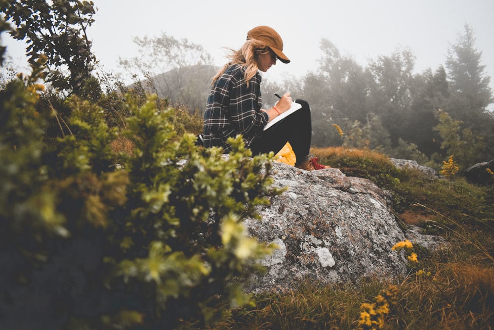 a woman sitting on top of a rock writing