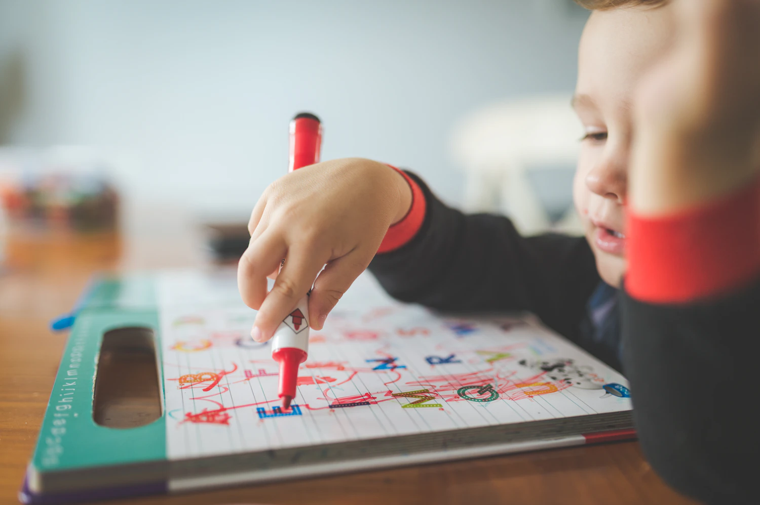 A young child coloring on paper with a crayon, marks going outside the shape