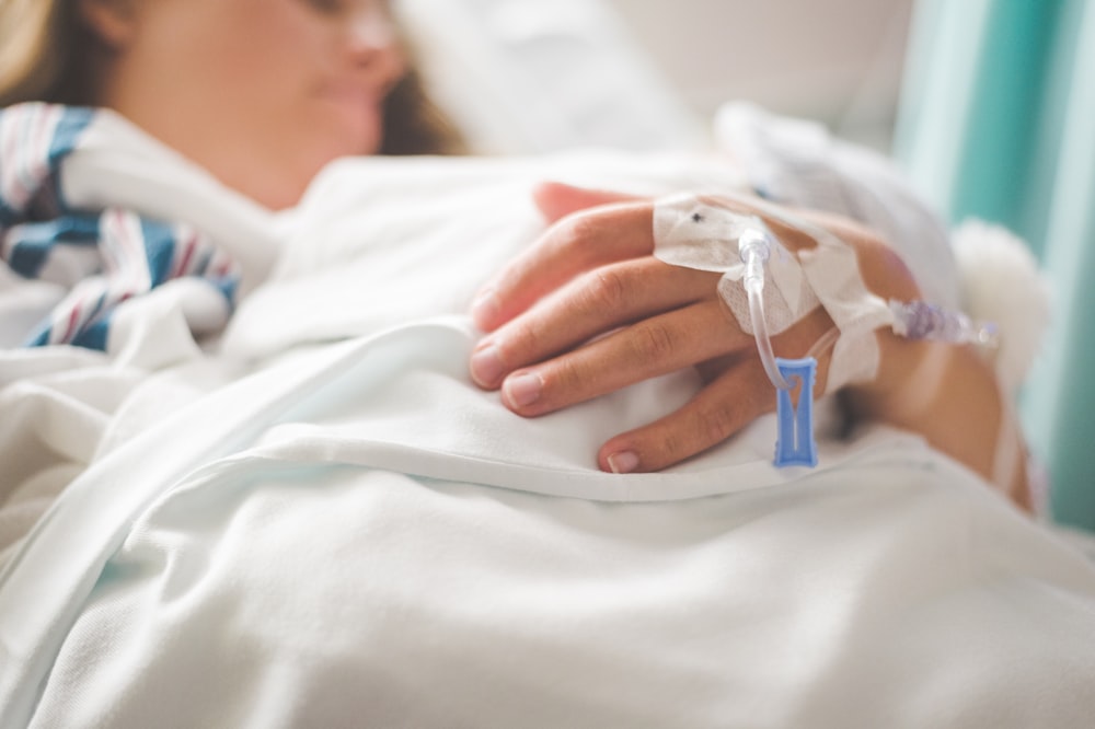 Una mujer acostada en una cama de hospital con una vía intravenosa en la mano