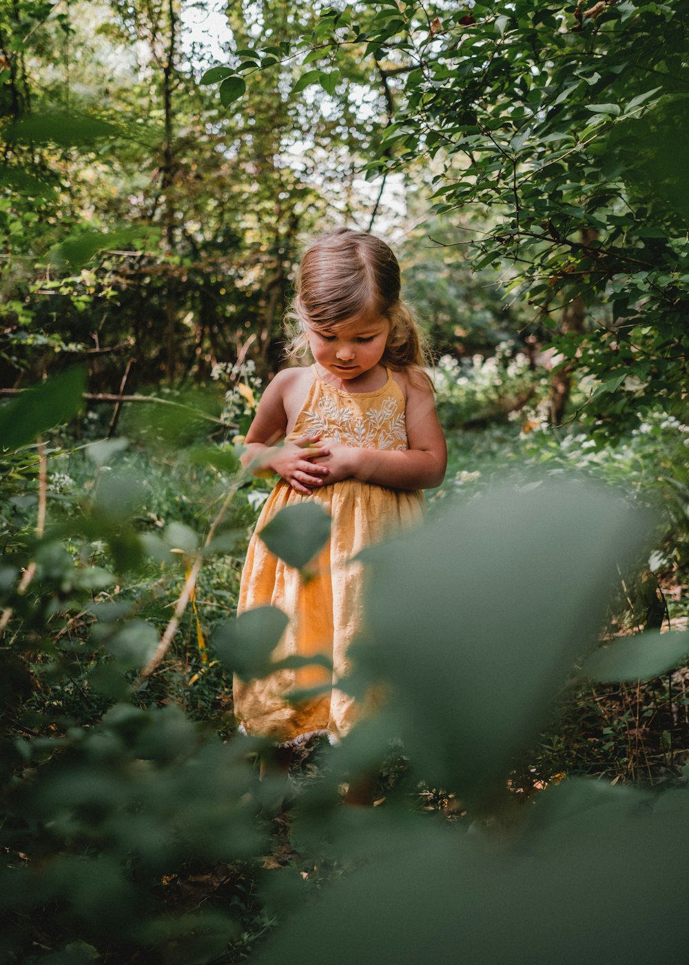 a little girl in a yellow dress standing in the woods