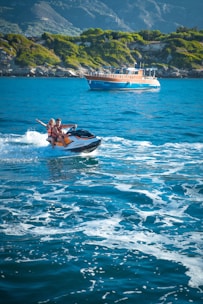 A couple riding jet skis side by side over sparkling ocean waves.