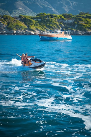 Thrilled tourists enjoying water sports, splashing through waves on jet skis against a bright sunny backdrop.