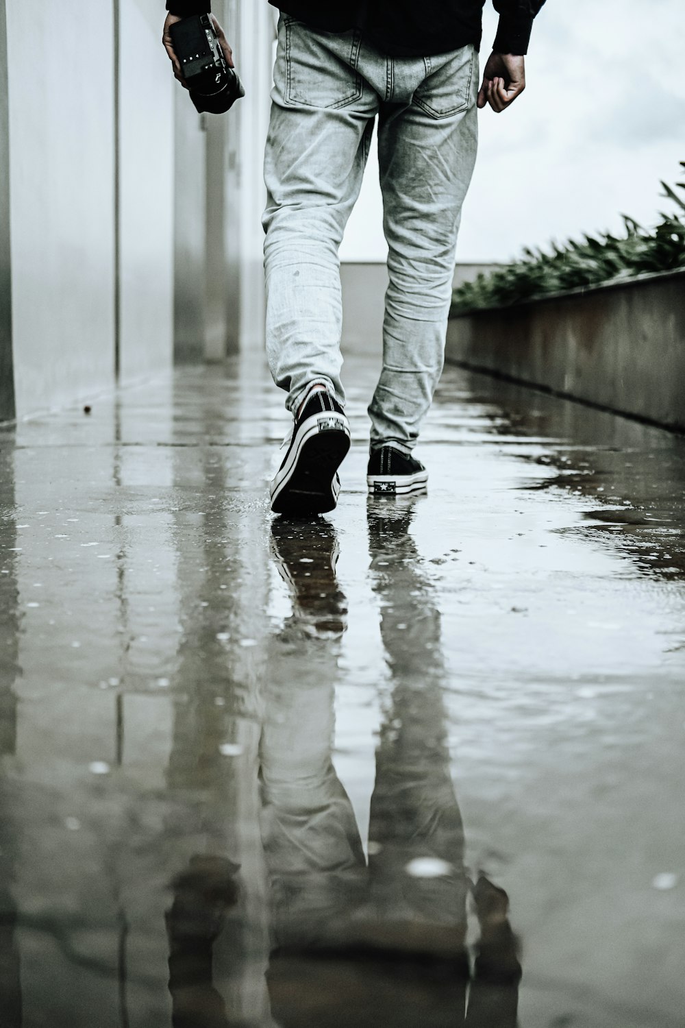 a man walking down a wet sidewalk holding an umbrella