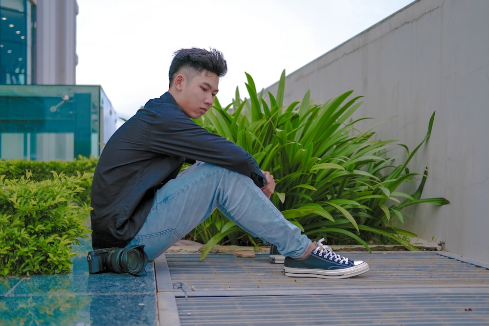 a man sitting on the ground next to a plant