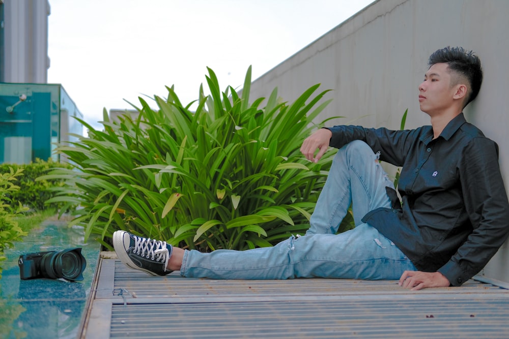 a man sitting on the ground next to a plant