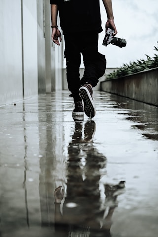 a man walking down a wet sidewalk holding a camera