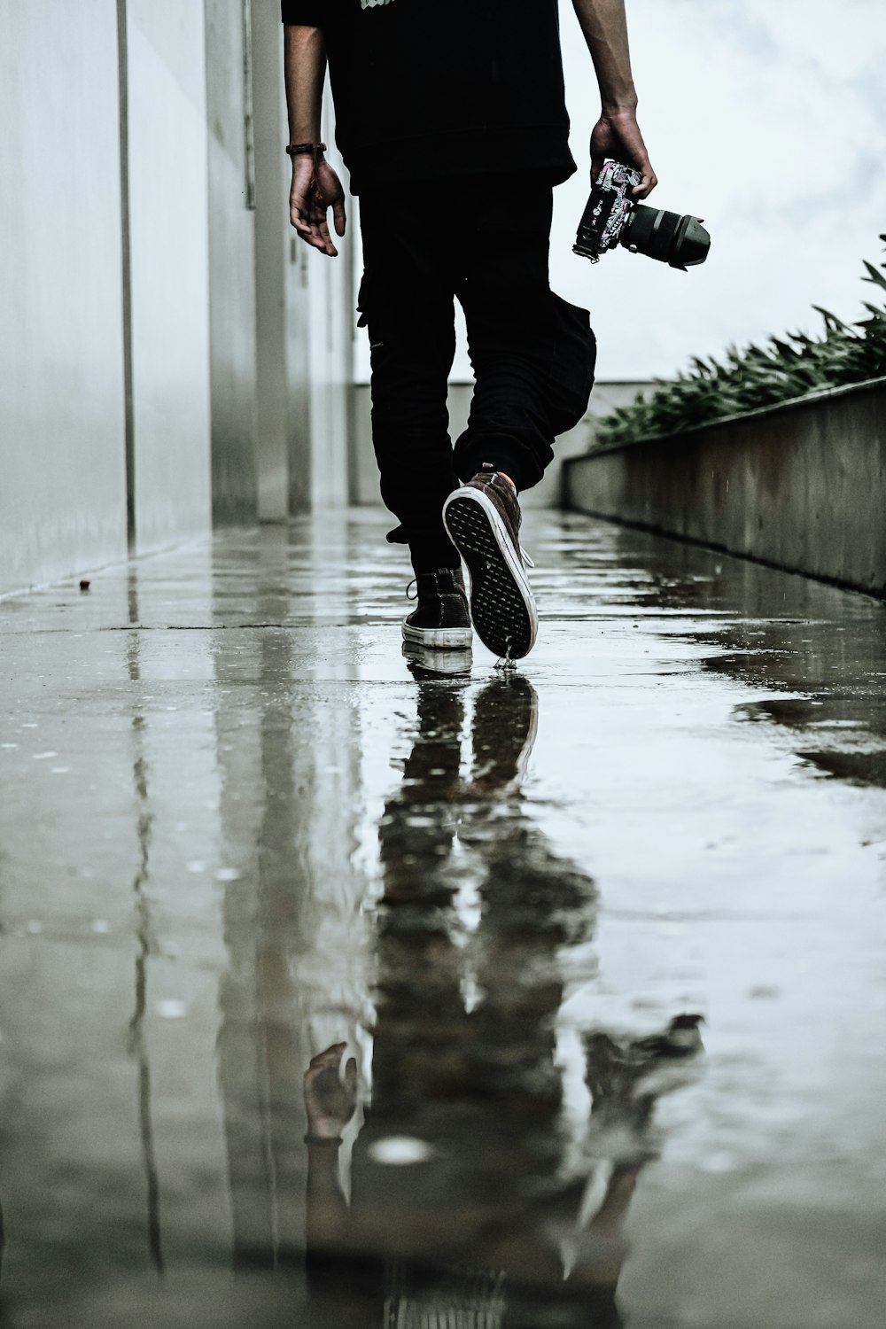 a man walking down a wet sidewalk holding a camera
