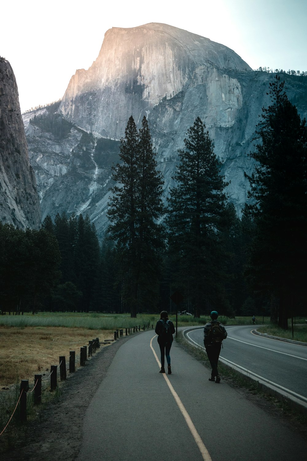 two people walking down a road in front of a mountain