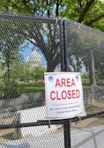 Government-grade mesh fencing neatly enclosing a public park area with visible signage.