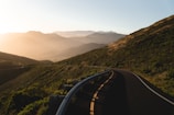 A scenic photo of a winding road through lush green hills during sunset