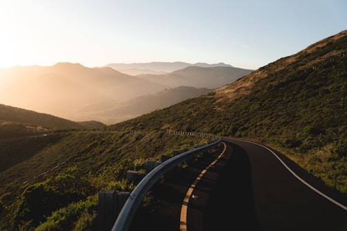 A scenic photo of a winding road through lush green hills during sunset