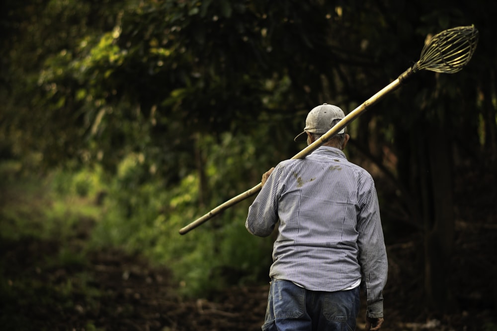 um homem com uma vassoura nas costas andando por uma estrada de terra