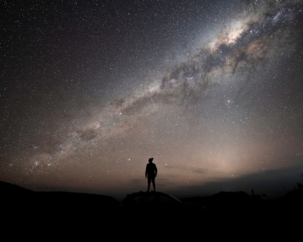a man standing on top of a hill under a night sky