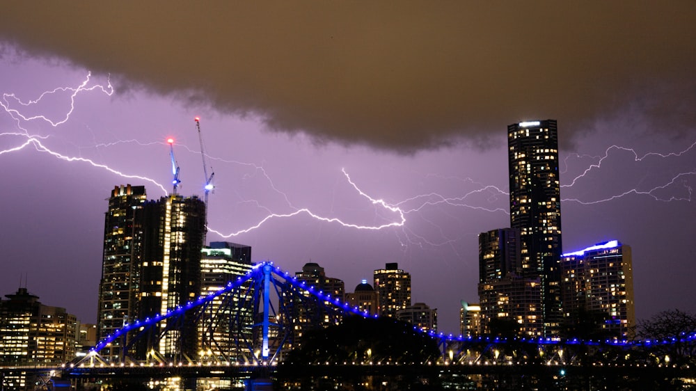 a city skyline with a bridge and lightning in the sky
