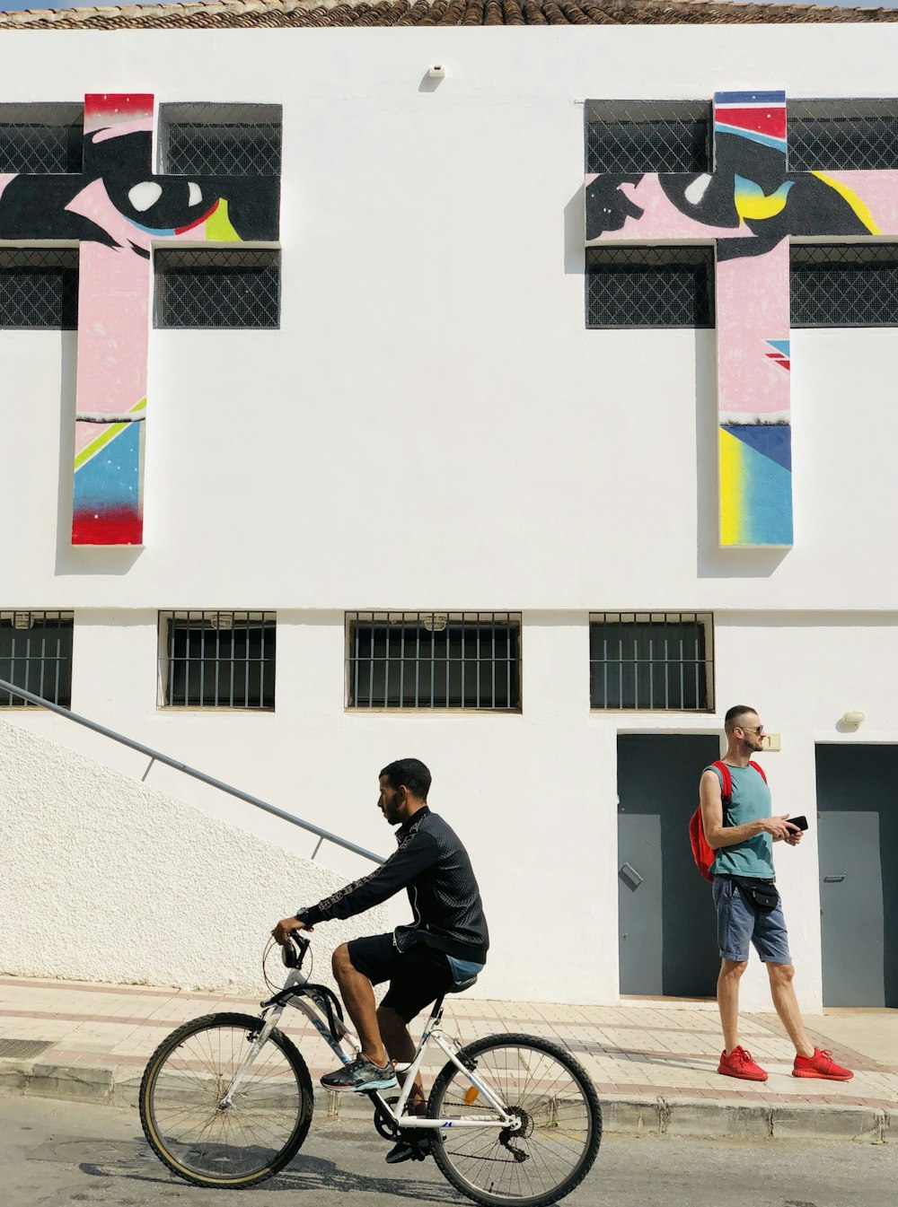 um homem andando de bicicleta por uma rua ao lado de um prédio alto