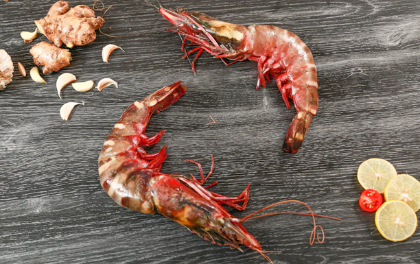 A happy customer unpacking a box of fresh tiger prawns in a bright kitchen.
