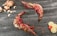 Two raw tiger prawns are placed on a dark wooden surface with scattered garlic cloves, ginger, lemon slices, and a red cherry tomato.