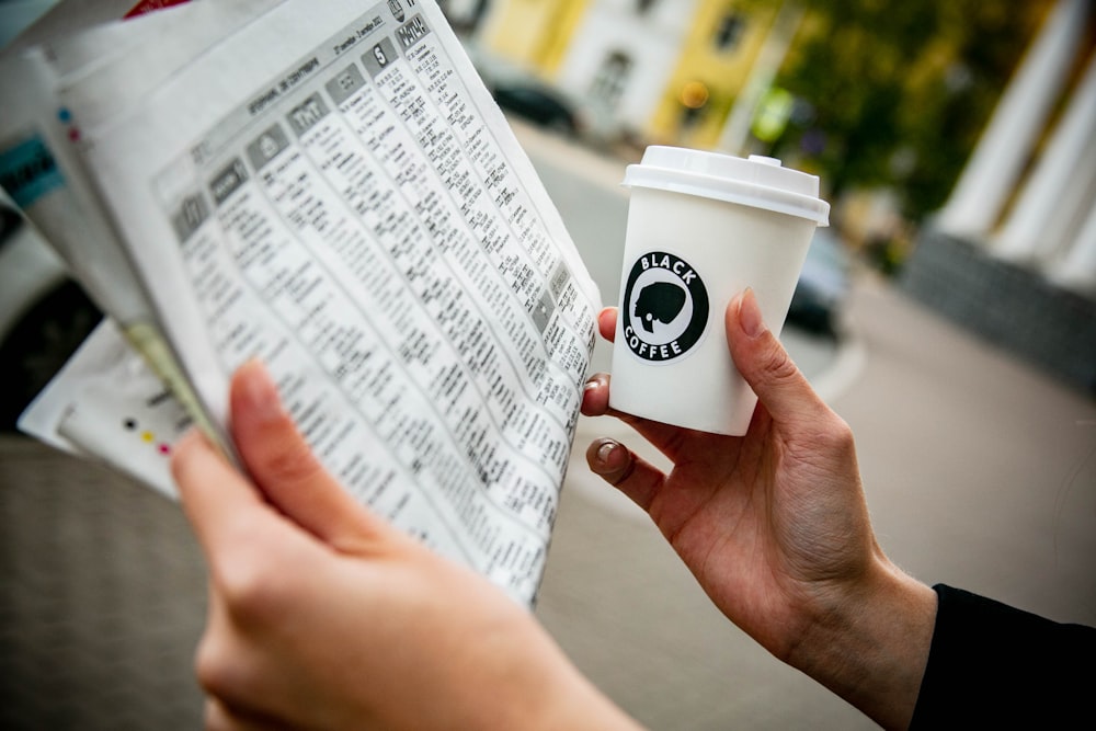 a person holding a cup of coffee and a newspaper