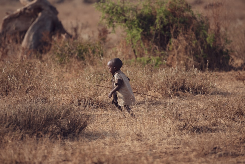 a young boy walking across a dry grass field