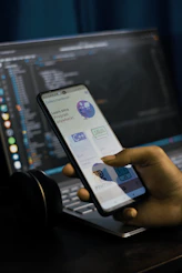 a person holding a cell phone in front of a laptop