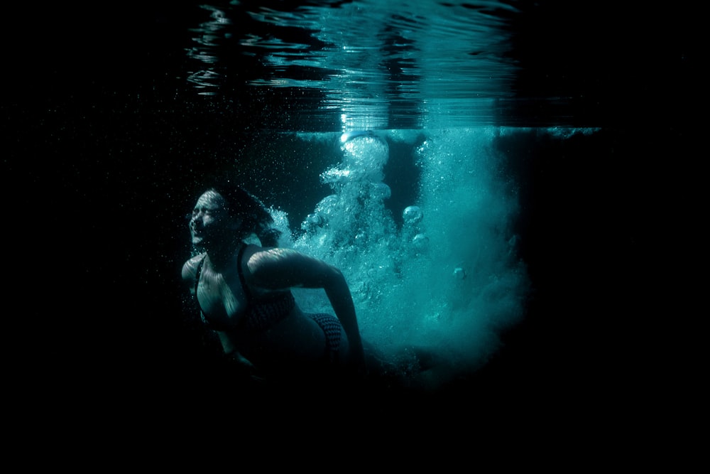 a woman in a bikini swims under water