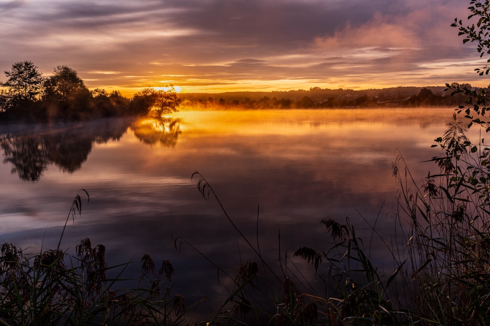 the sun is setting over a calm lake