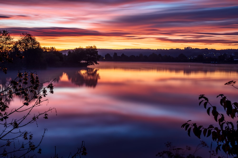 a beautiful sunset over a lake with trees in the foreground