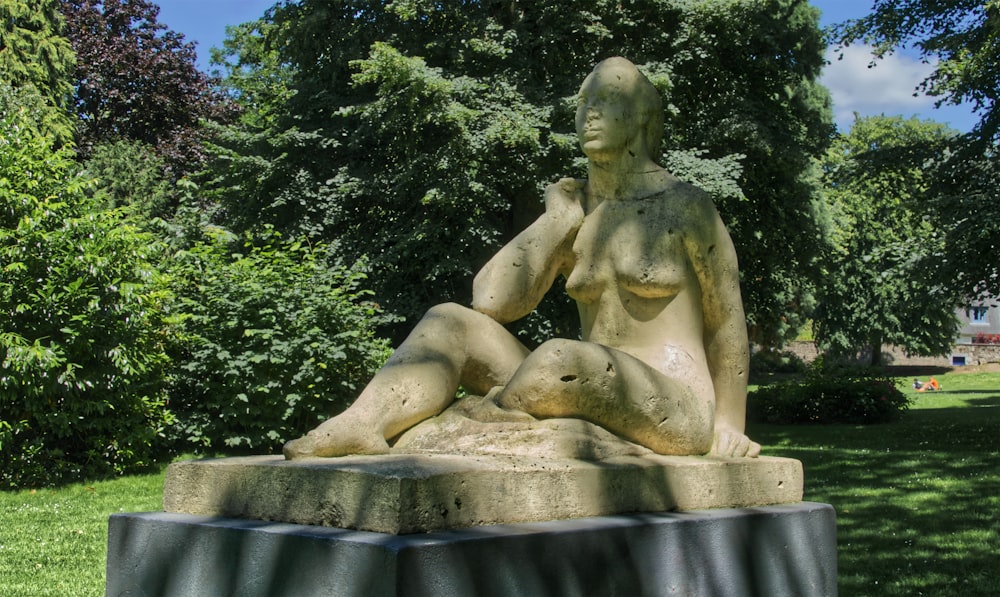 a statue of a woman sitting on a rock in a park