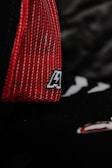 A close-up of a red mesh fabric with a sewn patch featuring a letter. The background is dark, adding contrast to the vivid red color.