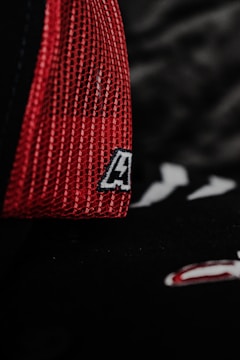 A close-up of a red mesh fabric with a sewn patch featuring a letter. The background is dark, adding contrast to the vivid red color.