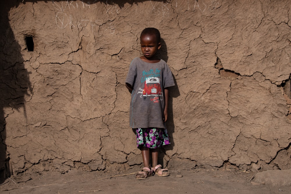 a little girl standing in front of a rock wall