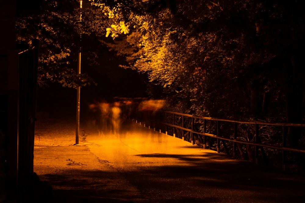 a dark street with a fence and trees in the background