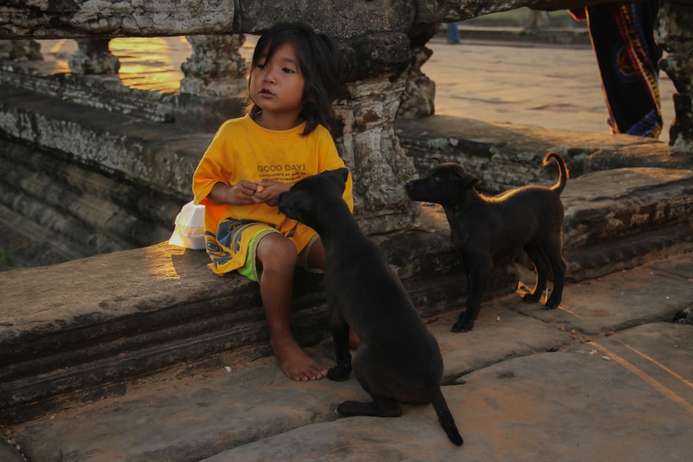a little girl sitting next to a black dog