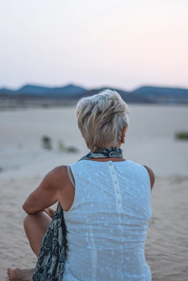 a woman sitting in the sand with her back to the camera