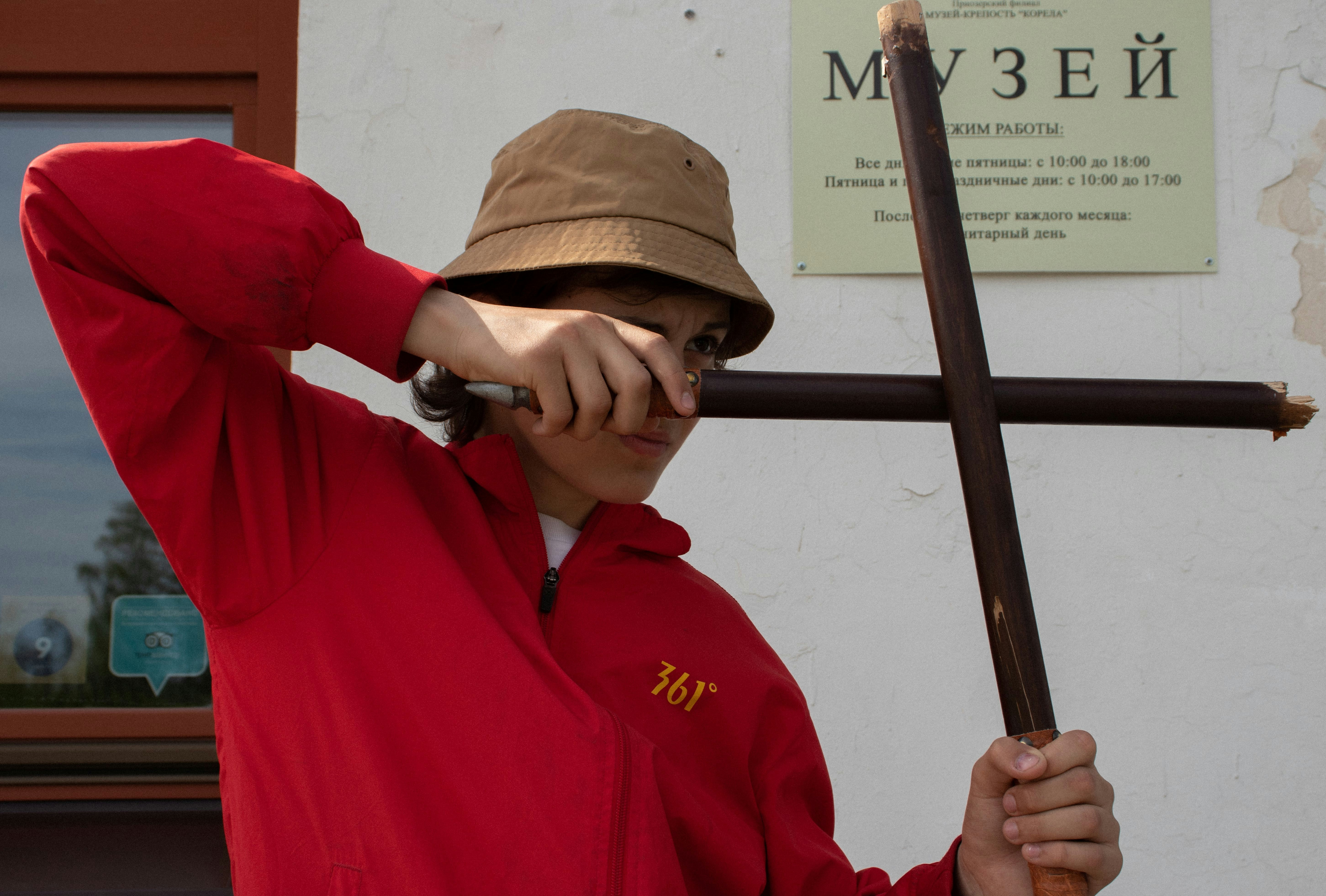 a woman in a red shirt and hat holding a stick