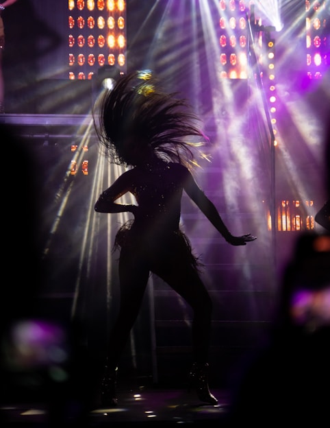 A dynamic photo of Irene Tassembedo performing a powerful dance on stage, illuminated by warm spotlight.