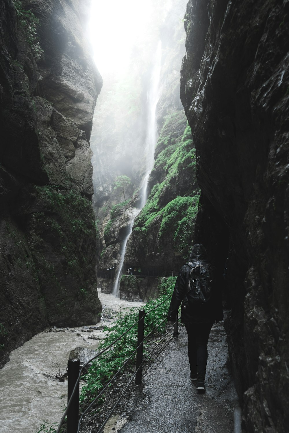 a person with a backpack walking down a path near a waterfall