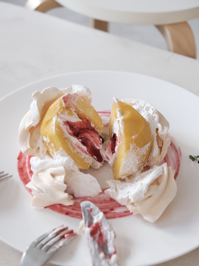 A meringue and cream dessert filled with peaches, split open on a plate