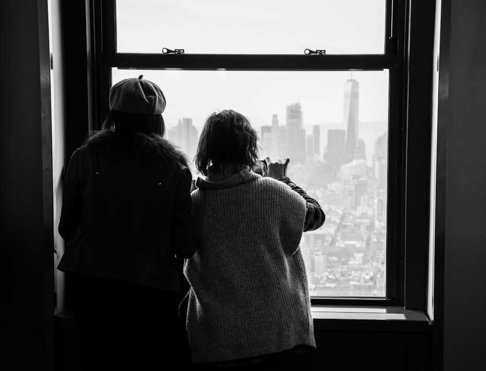 two women looking out a window at a city