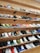 A variety of colorful sneakers neatly organized on several wooden shelves attached to a wall. The sneakers come in different designs and color combinations, showcasing a diverse collection suitable for display or sale in a retail environment.