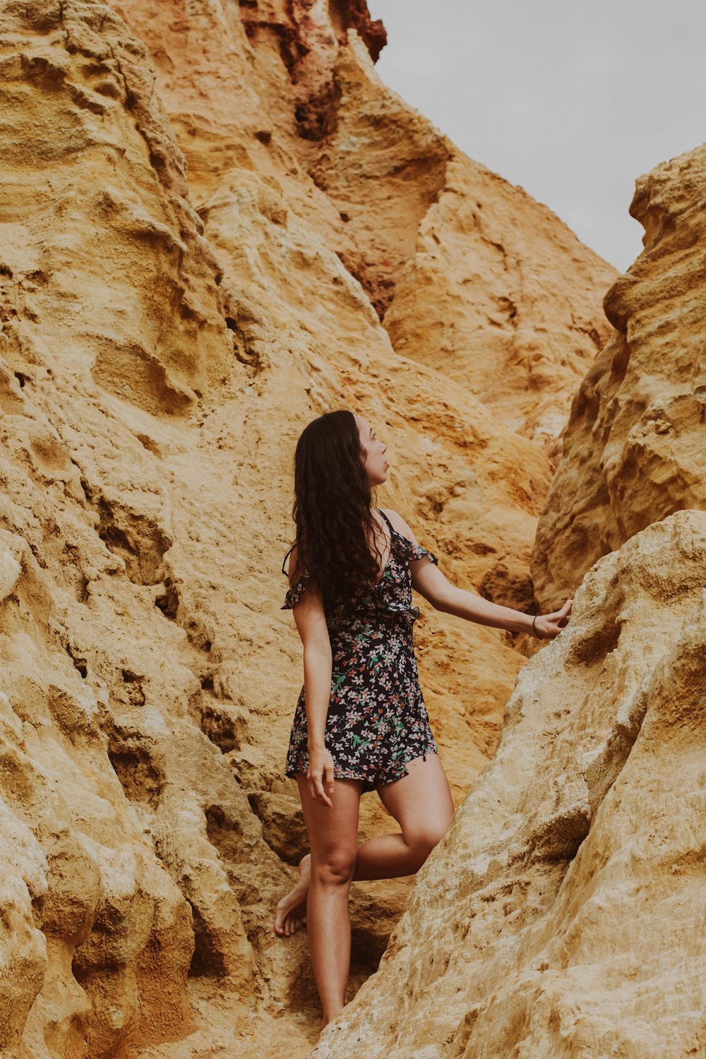 a woman climbing up a rocky cliff in a dress