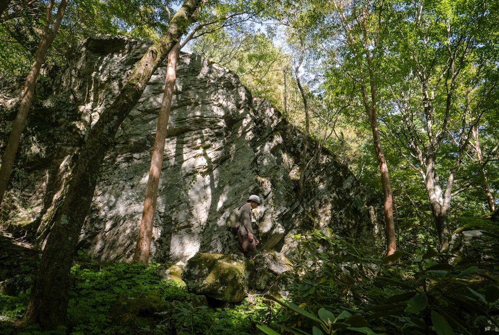 a man standing in front of a large rock in the woods