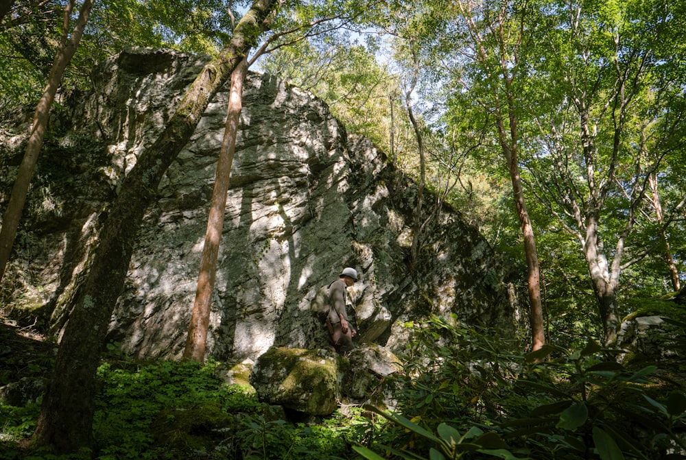 Un uomo in piedi di fronte a una grande roccia nel bosco