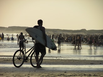 a man carrying a surfboard and a bike on a beach