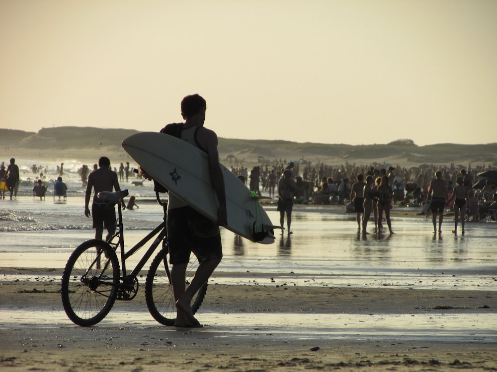 a man carrying a surfboard and a bike on a beach
