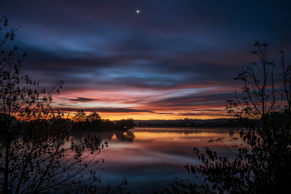 a sunset over a body of water with trees in the foreground