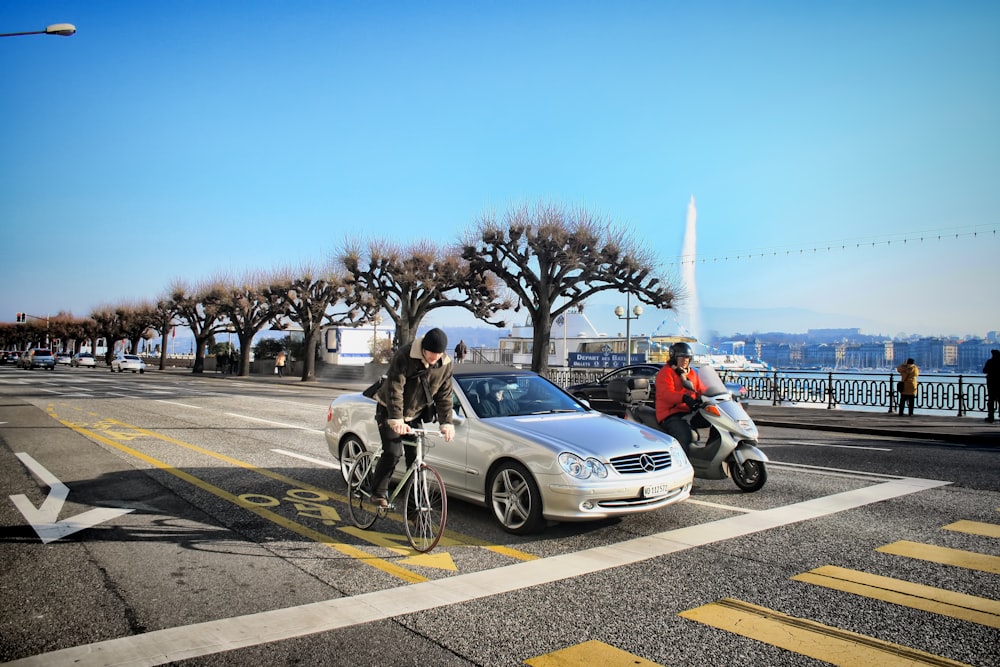 a man riding a bike next to a silver car