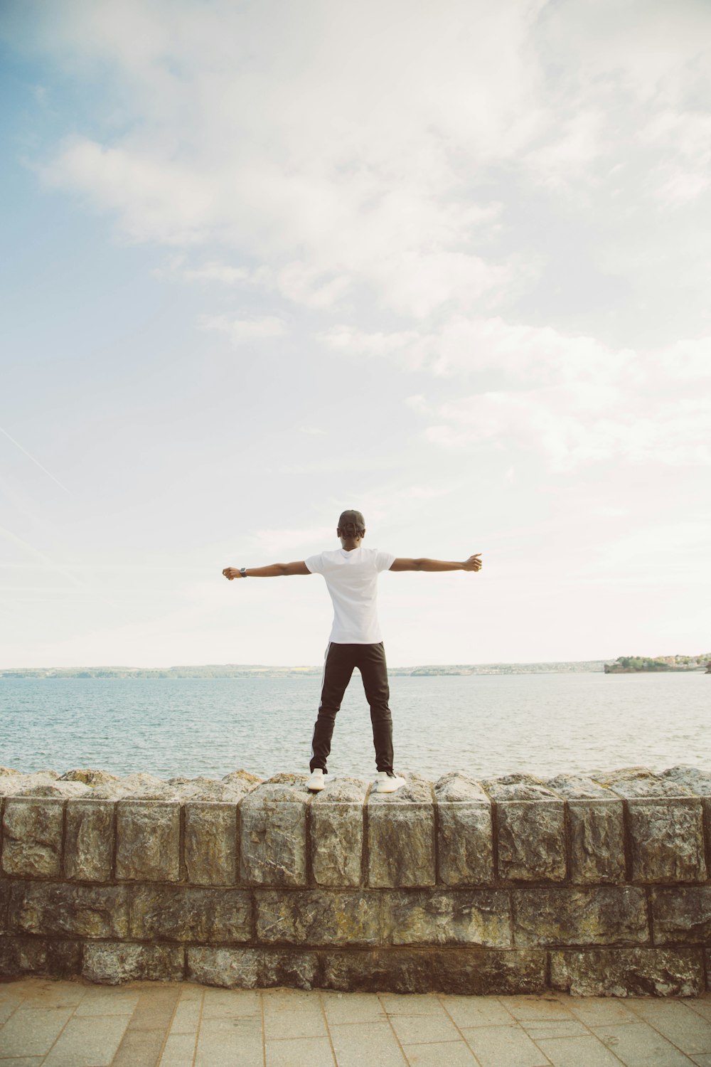 a man standing on a stone wall near the ocean